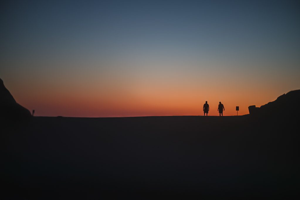 Two figures silhouetted on a dune ridge at dusk