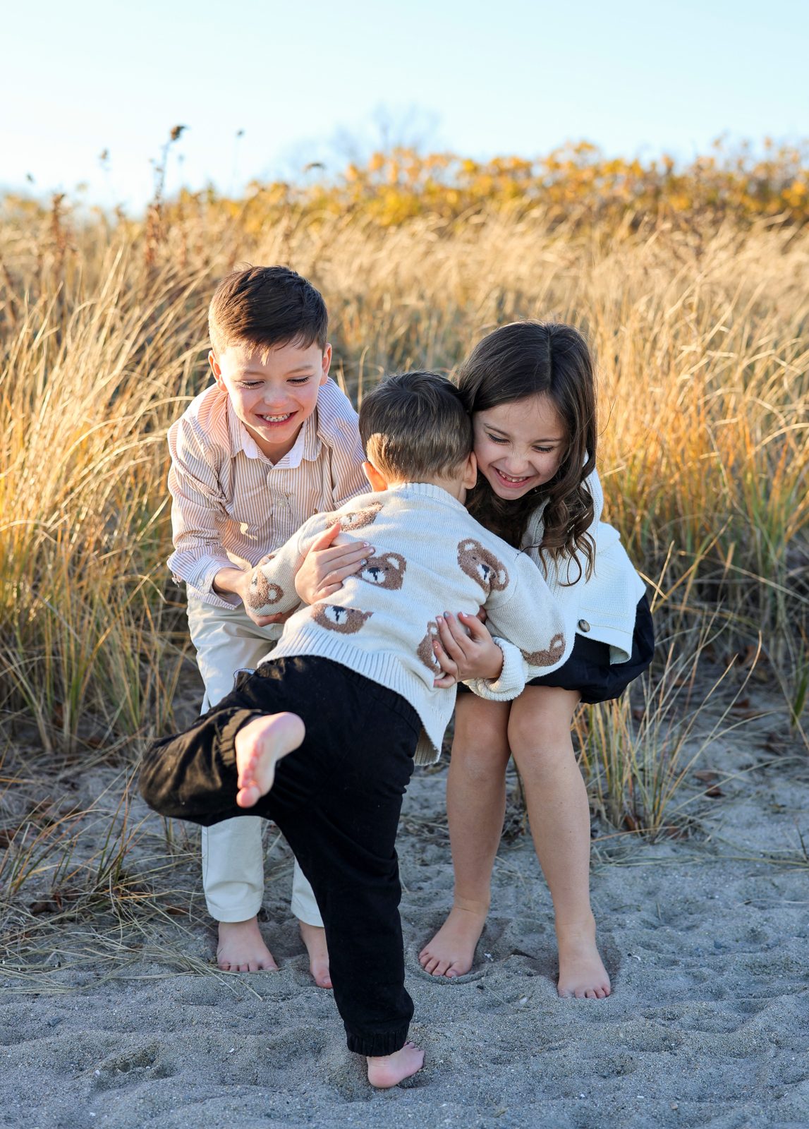 Three children laughing in golden dune grass at sunset