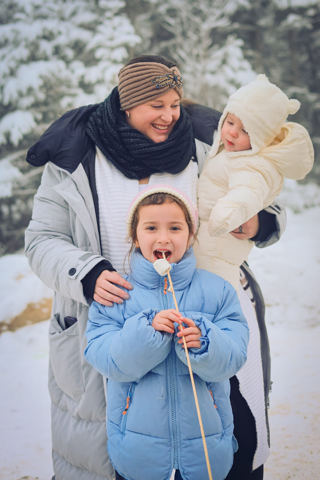 Mom and kids sharing marshmallows in a snowy pine forest