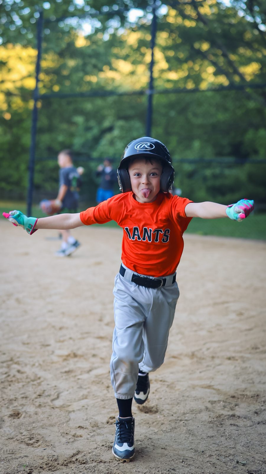 Young ballplayer celebrating with arms out and tongue out, running down the baseline
