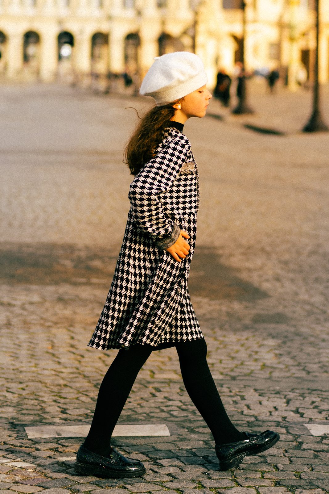 Girl in houndstooth coat crossing a cobblestone square